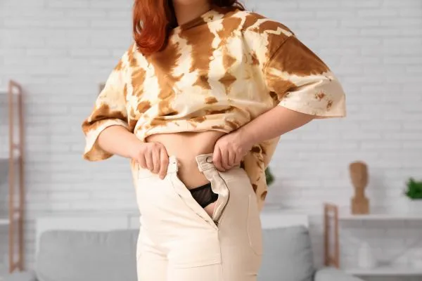 Image of woman trying to do her trousers up after pregnancy weight gain Tipton
